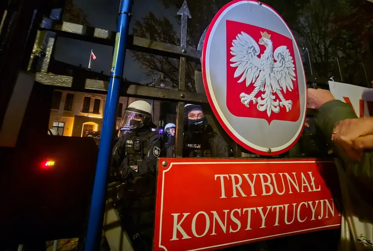 Znak Trybunału Konstytucyjnego i funkcjonariusze policji zabezpieczający teren wokół budynku TK w Warszawie. Fot. PAP/Radek Pietruszka